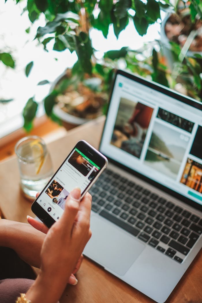 A cozy workspace featuring a smartphone and laptop used for social networking surrounded by greenery.