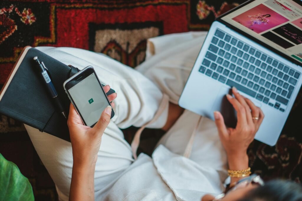 A woman using a smartphone and laptop simultaneously for digital tasks.