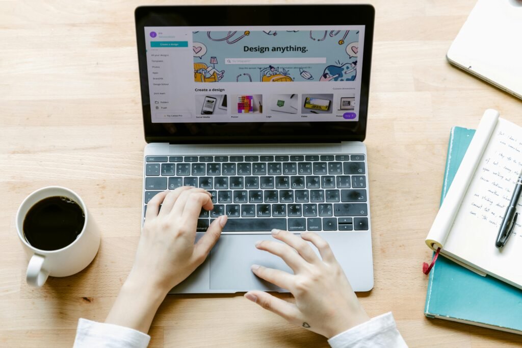 From above anonymous person typing on laptop while sitting at table and working on design project in contemporary workspace with notebook